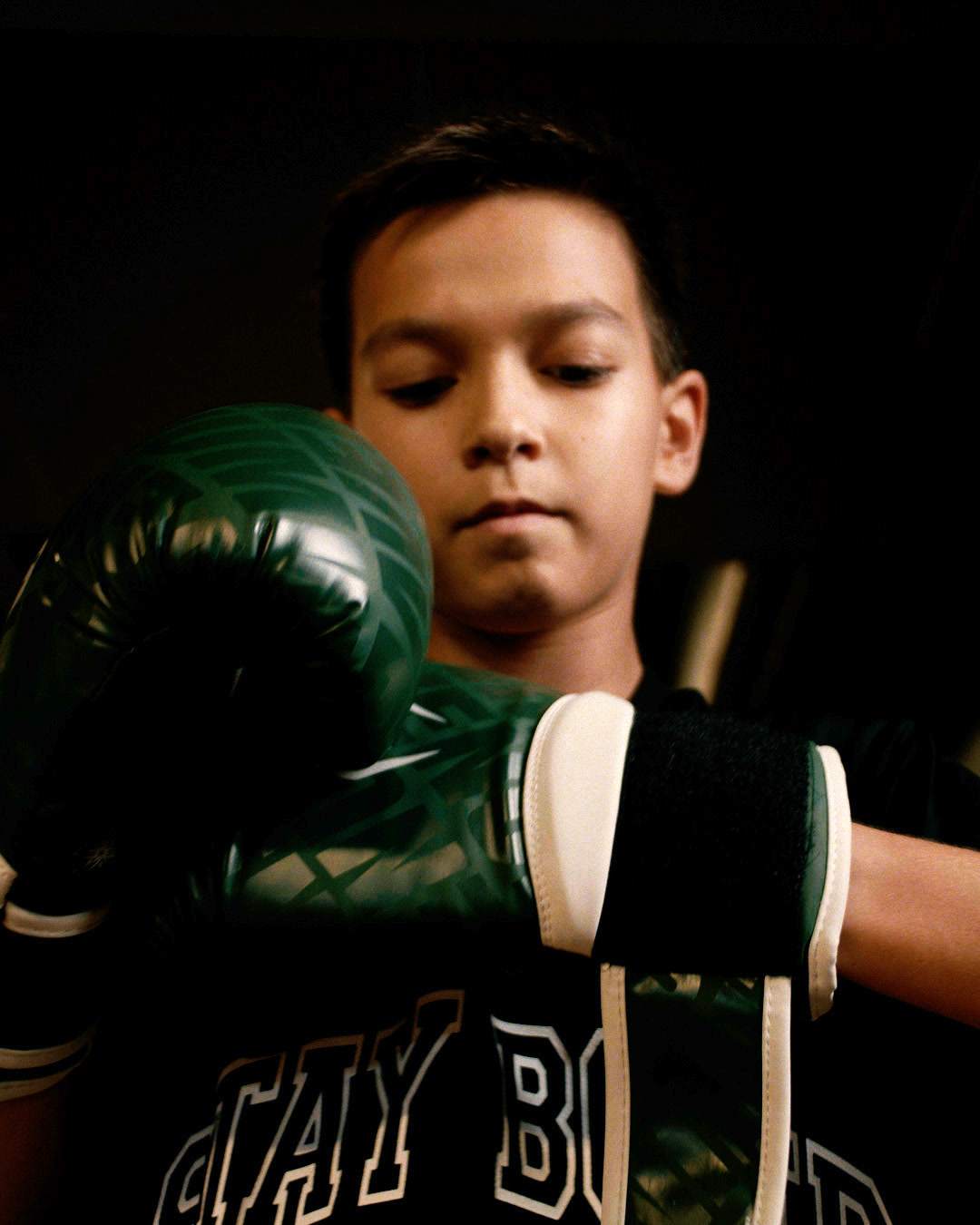 A boy puts on green boxing gloves.