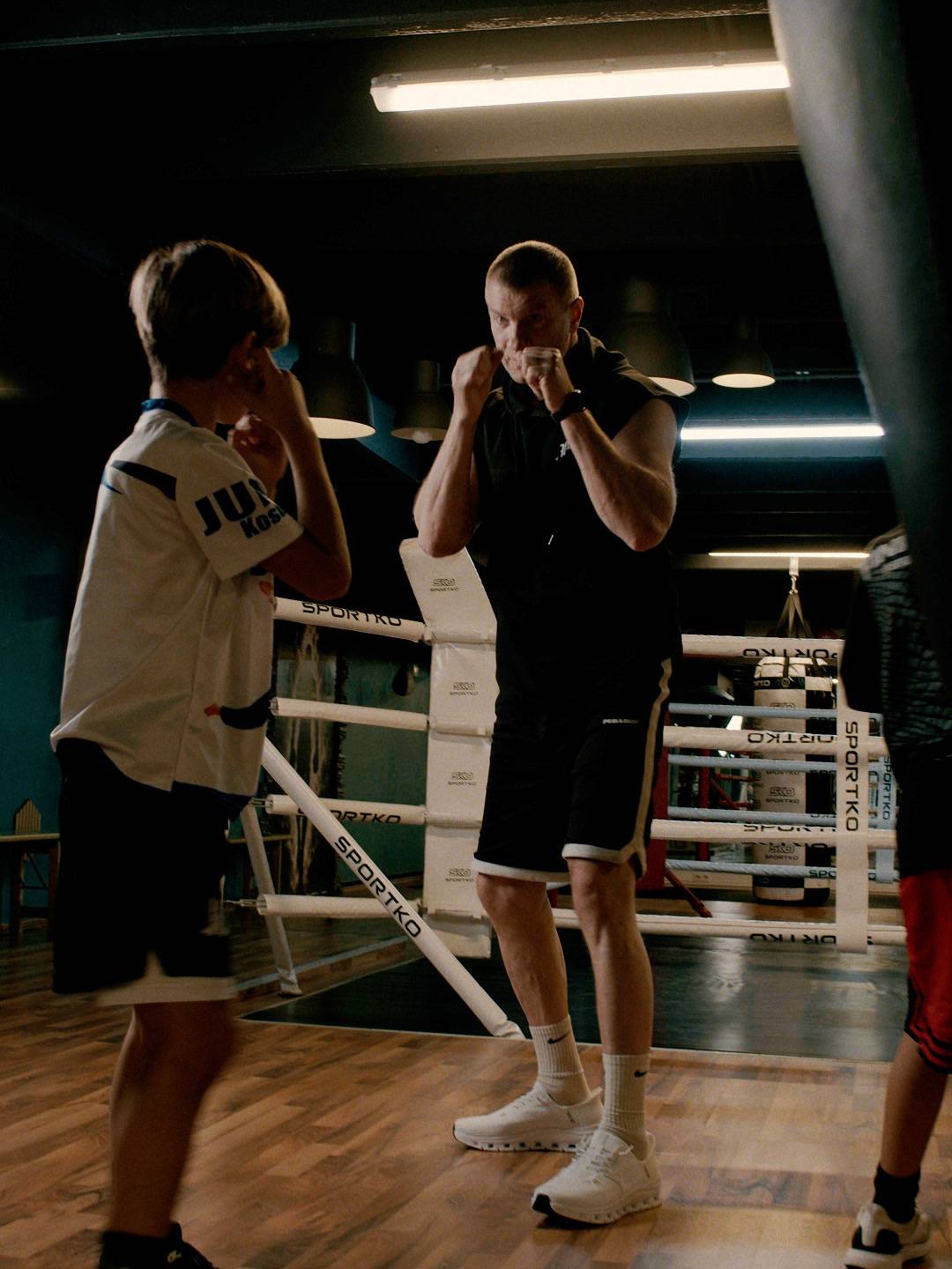A coach and a boy face each other in the ring with their guard up.