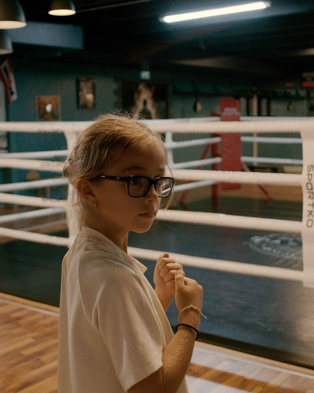 A girl with glasses stands next to the ring in a boxing stance.
