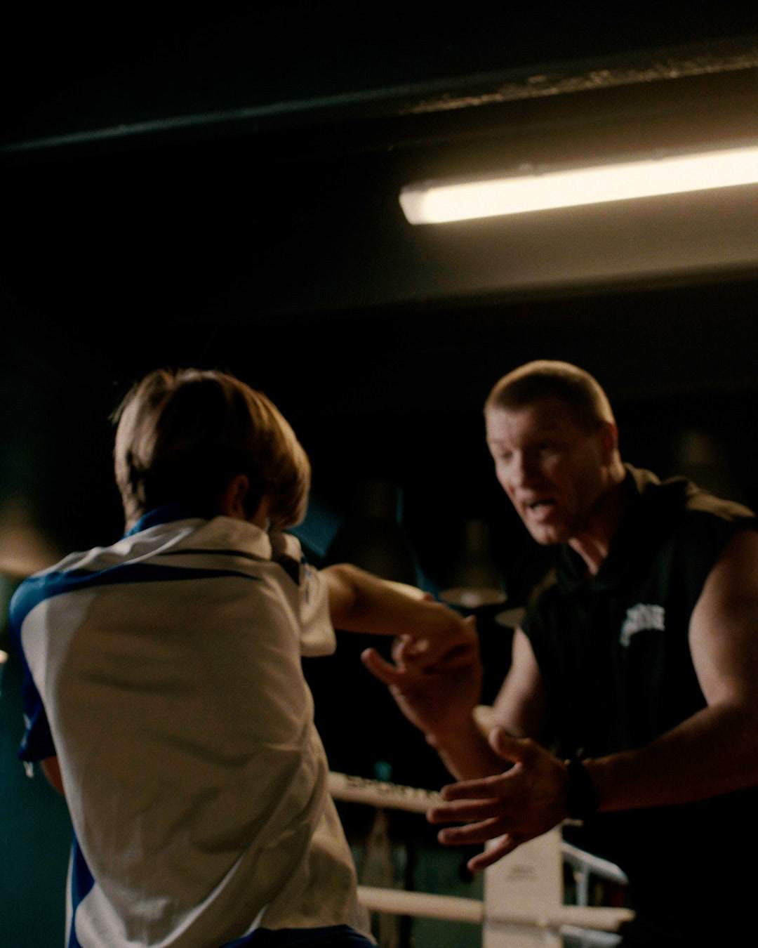 The coach corrects a boy’s punching technique by the ring.
